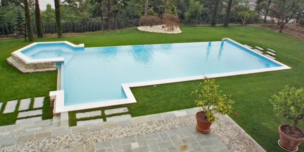 Piscina interrata con sfioro a cascata, forma libera su dislivello in giardino.