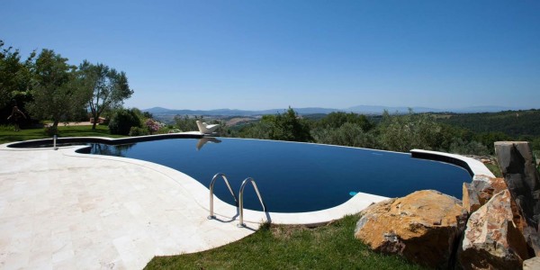 Piscina interrata panoramica con sfioro a cascata, forma libera su terrazza.