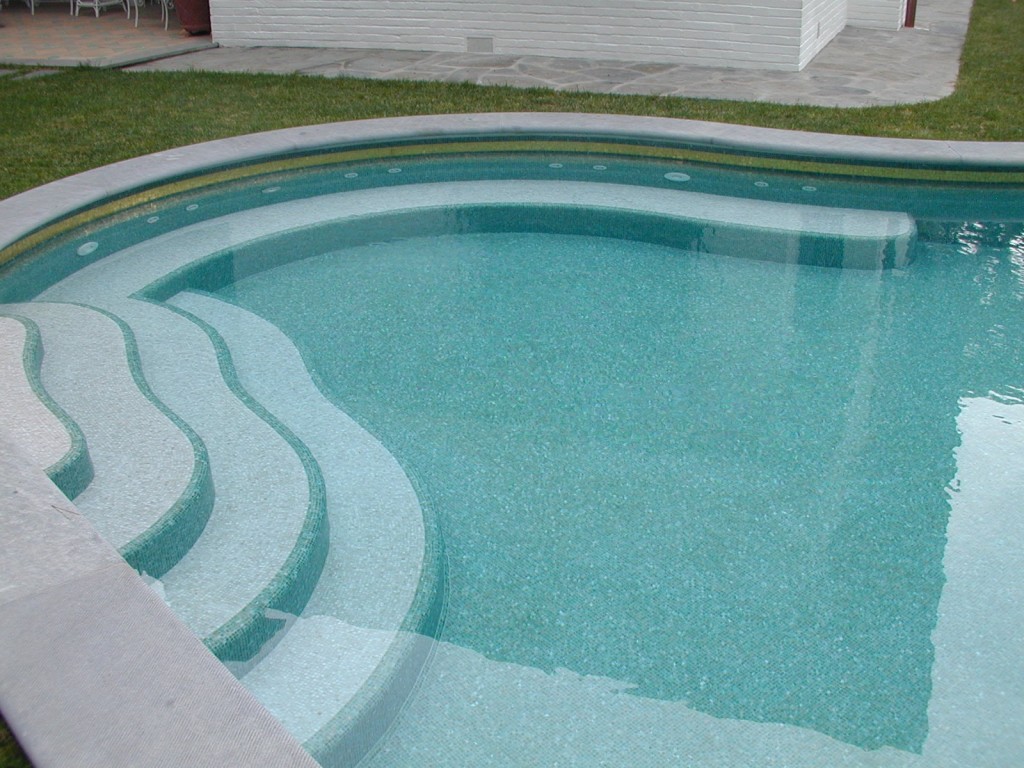 Piscina interrata in cemento armato con scale a forma libera e fondo in mosaico.