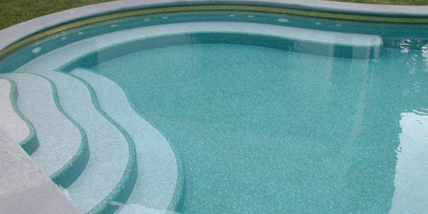 Piscina interrata in cemento armato con scale a forma libera e fondo in mosaico.