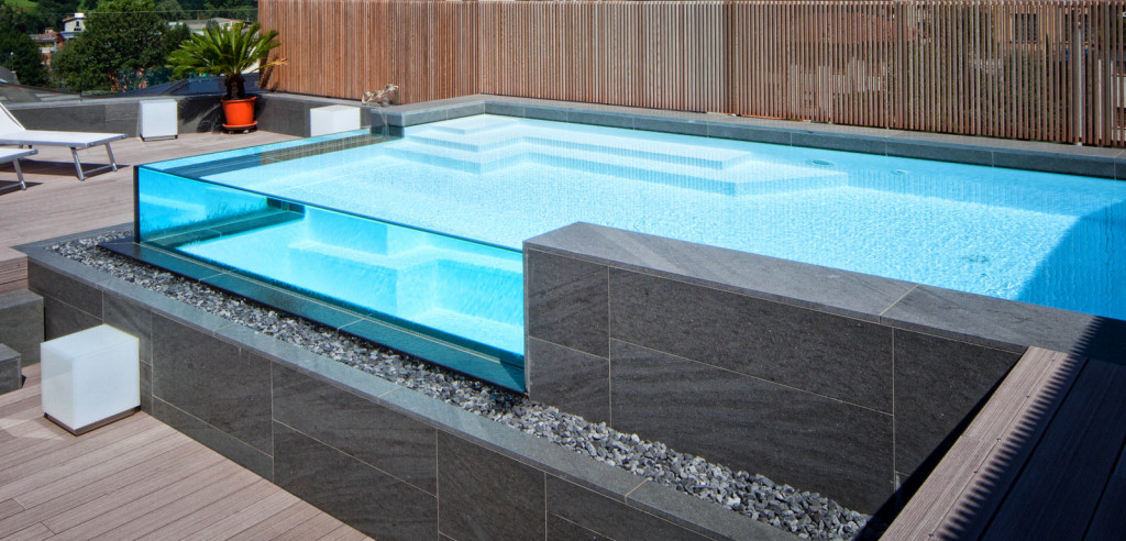 Piscina semi-interrata con Sfioro a cascata Crystal in metacrilato, con gradini e griglia a ghiaia.
