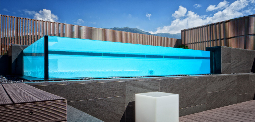 Piscina semi-interrata con Sfioro a cascata Crystal in metacrilato, con gradini e griglia a ghiaia.