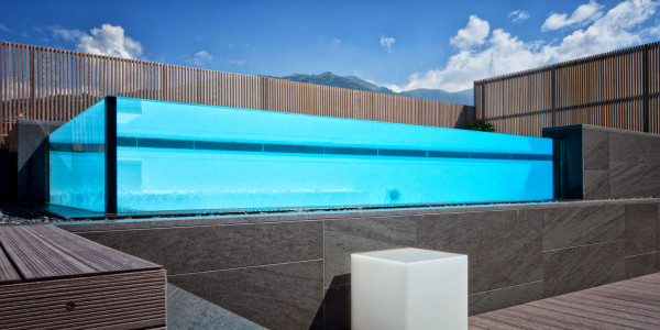 Piscina semi-interrata con Sfioro a cascata Crystal in metacrilato, con gradini e griglia a ghiaia.