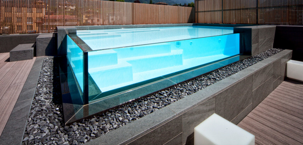 Piscina semi-interrata con Sfioro a cascata Crystal in metacrilato, con gradini e griglia a ghiaia.