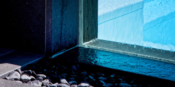 Piscina semi-interrata con Sfioro a cascata Crystal in metacrilato, con gradini e griglia a ghiaia.