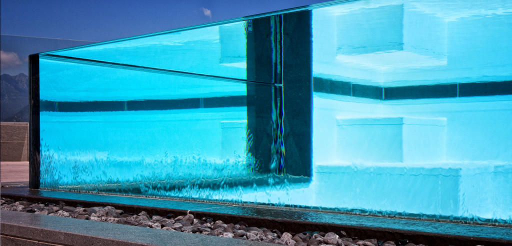 Piscina semi-interrata con Sfioro a cascata Crystal in metacrilato, con gradini e griglia a ghiaia.