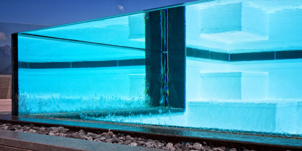 Piscina semi-interrata con Sfioro a cascata Crystal in metacrilato, con gradini e griglia a ghiaia.