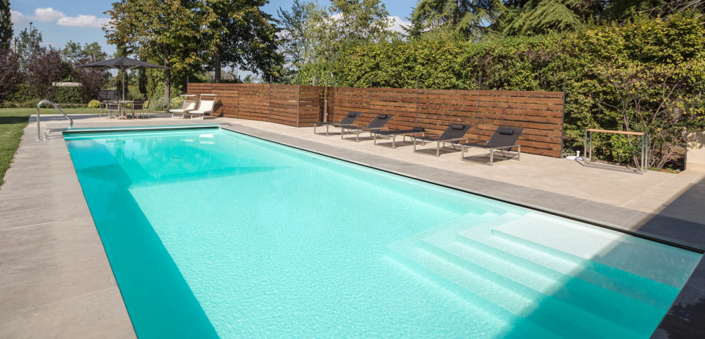 Piscina interrata esterna con bordo a sfioro nascosto Freedom e scale ad angolo.